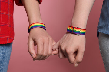 LGBT concept. Women in rainbow wristbands holding hands on pink background, closeup