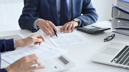 Accountants analyzing financial documents, calculating numbers together at shared workspace with...
