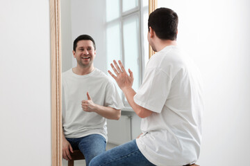 Man sitting in front of mirror where his reflection showing thumbs up indoors. Mental health