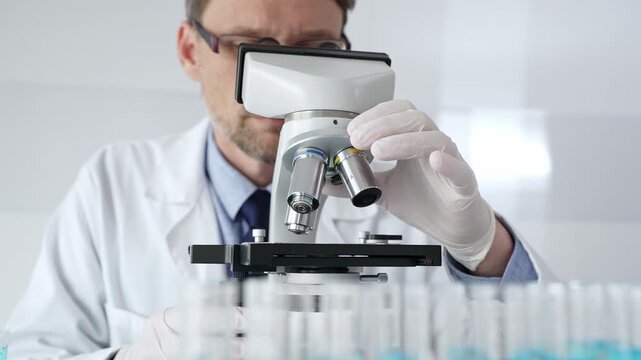 Man scientific researcher wearing white protective gloves carefully calibrating laboratory microscope, performing precision medical investigation. Medicine, healthcare and science concept
