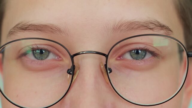 A cheerful young woman in round glasses looks at the camera and smiles in close-up. The happy look of a young girl with grey eyes.