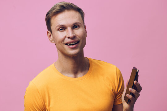 smiling man hold smartphone use mobile phone casual yellow t-shirt pink background digital nomad concept technology communication wireless connection