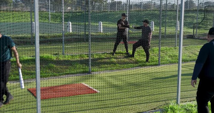 Feeder tossing balls, pitching machine firing, batter swinging bat in cage for practice, copy space