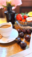 Creamy coffee alongside scattered cherries, ripe strawberries, figs on white saucer, complemented by soft pink rose petals in soft focus background