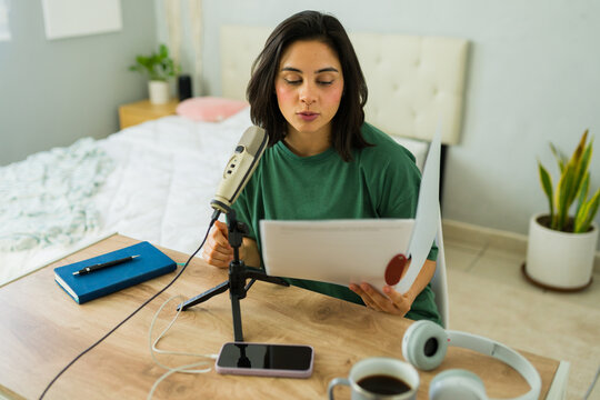 Young woman recording a podcast from home using a microphone and smartphone
