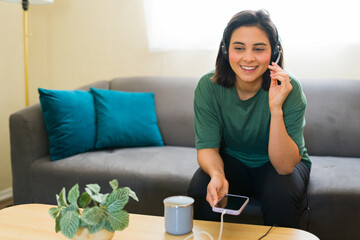 Happy latin woman working from home using smartphone and headset