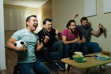 Group of friends watching football game at home, drinking beer and celebrating goal