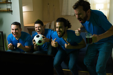 Excited male friends cheering while watching soccer match at home