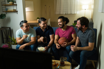 Cheerful friends watching basketball game on tv, drinking beer and eating snacks