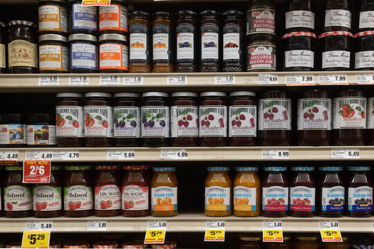 Davis, CA, USA. 11 August 2025. Supermarket store shelf with various brands of preerve and jams, with price tags underneath of them