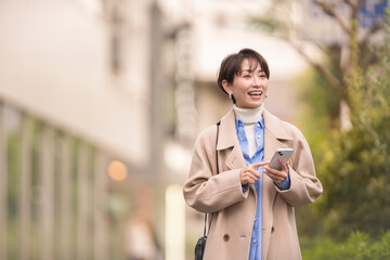 スマートフォンを持ち街中を歩く女性。