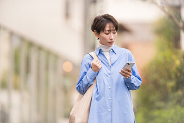 スマートフォンの画面をみながら街中を歩く女性。