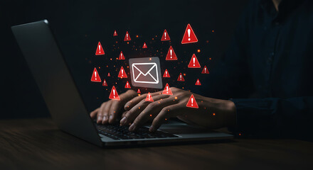 Hacker using a laptop with glowing red alert icons and an email symbol emanating from the screen