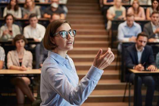 Confident female speaker presenting to audience in lecture hall, public speaking, education, leadership.