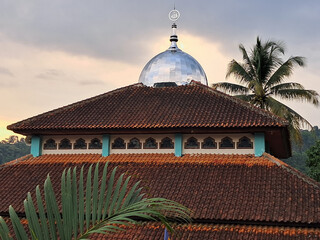 Traditional mosque with tiled roof and silver dome at sunset