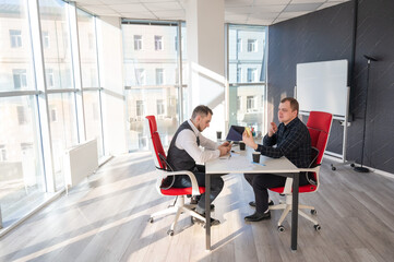 Two Caucasian men using smartphones while sitting at a desk. 