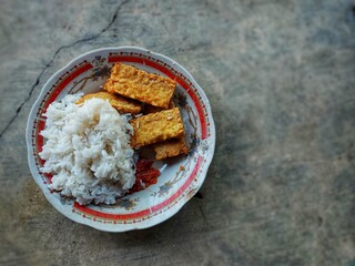 Fried tempeh with white rice and chilies served on a white plate. Tempeh, a traditional Indonesian...