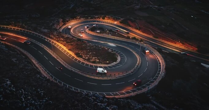 Malta: Aerial view cars driving at night on a winding road, creating a visually striking s-shaped pattern illuminated by streetlights. Drone flight footage