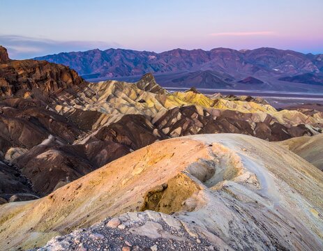 Colorful, eroded desert landscape at sunrise, showcasing layered rock formations and distant mountain range - Powered by Adobe