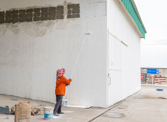 Construction worker painting the exterior wall of a building with white paint using a long roller brush.
