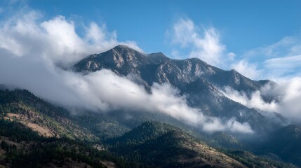 Majestic mountain range covered with mist and clouds under a bright blue sky, creating a breathtaking natural landscape perfect for travel, adventure, and nature backgrounds.