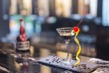 Cocktail with orange peel and red cherry on martini glass in club