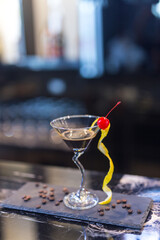Cocktail with orange peel and red cherry on martini glass in club