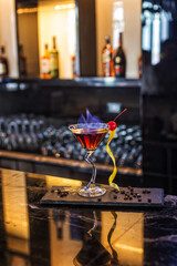 Cocktail with orange peel and red cherry on martini glass in club