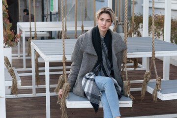 young beautiful woman posing in coat on swing