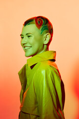 Young woman with colorful hairstyle and bright yellow coat smiling against orange background,...