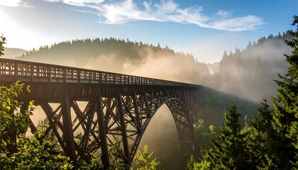 Obraz premium Misty sunrise illuminates a long wooden arch bridge high above a valley shrouded in fog, with evergreen trees