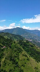 Obraz premium Lush green mountain slopes ascend to a clear blue sky, dotted with fluffy white clouds