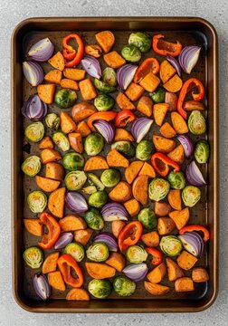 Overhead view of roasted vegetables on a baking sheet with sweet potatoes and brussels sprouts and red onions