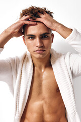 Stylish young man in a white robe looking directly at the camera, with a confident expression. Indoor portrait showcasing modern fashion and self-confidence.