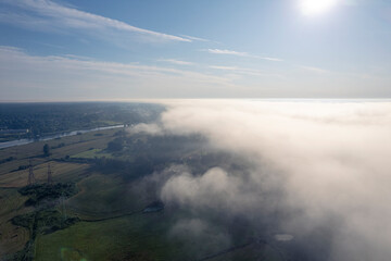 Aerial photo above the fog or white clouds with shining sun. Beautiful sunrise cloudy sky from aerial view. Above clouds from airplane window or drone.