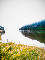 Fog at dawn. The forest, reflected in the lake, dissolves on the horizon, turning into a pale sky.