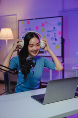 Young happy asian woman wearing headphones using microphone and laptop recording podcast or online...