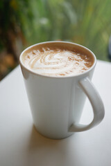 Coffee cup on a table with greenery behind