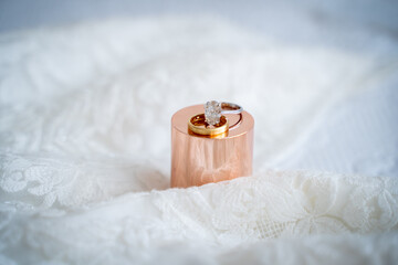 Close up of wedding rings on golden stand with lace background.