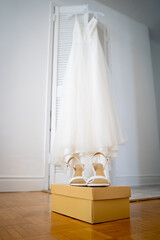 White bridal shoes on box with wedding dress in background.