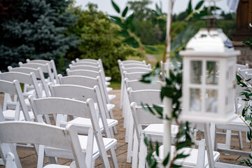 Outdoor wedding ceremony setup with white chairs and lantern decorations.