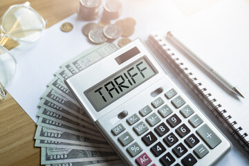 Tariff calculation concept with calculator displaying the word tariff, US dollar bills, coins,...