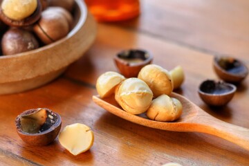 Shelled Macadamia (Macadamia integrifolia) in wooden spoon and some seed in bowl on wooden table.Favorite for snack and very delicious.Have a lot of unsaturated fatty acid.Selective focus.