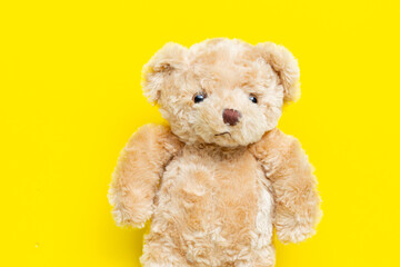 Cute brown teddy bear plush toy on yellow background.