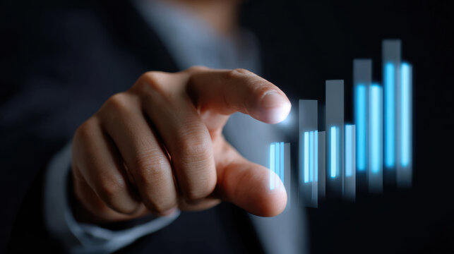 Businessman hand pointing at glowing blue bar graph with import, traffic, and trade concepts in dark background