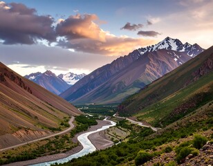 Serpentine river meanders through a valley between majestic, snow-capped mountains under a dramatic sunset sky