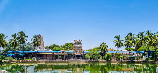 A picturesque view of the Pillaiyarpatti temple in Tamil Nadu, showcasing its vibrant gopurams, serene temple pond, coconut trees that highlight the rich cultural and architectural heritage of india