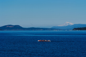 A red rowing boat glides across the ocean near Sidney, Vancouver Island, with distant mountains and...