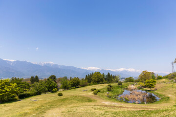 北アルプスを望むあづみ野池田クラフトパークの池と草原風景