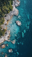 Fototapeta premium High-angle view of a rocky shoreline meeting turquoise water. Lush green trees line the cliffs
